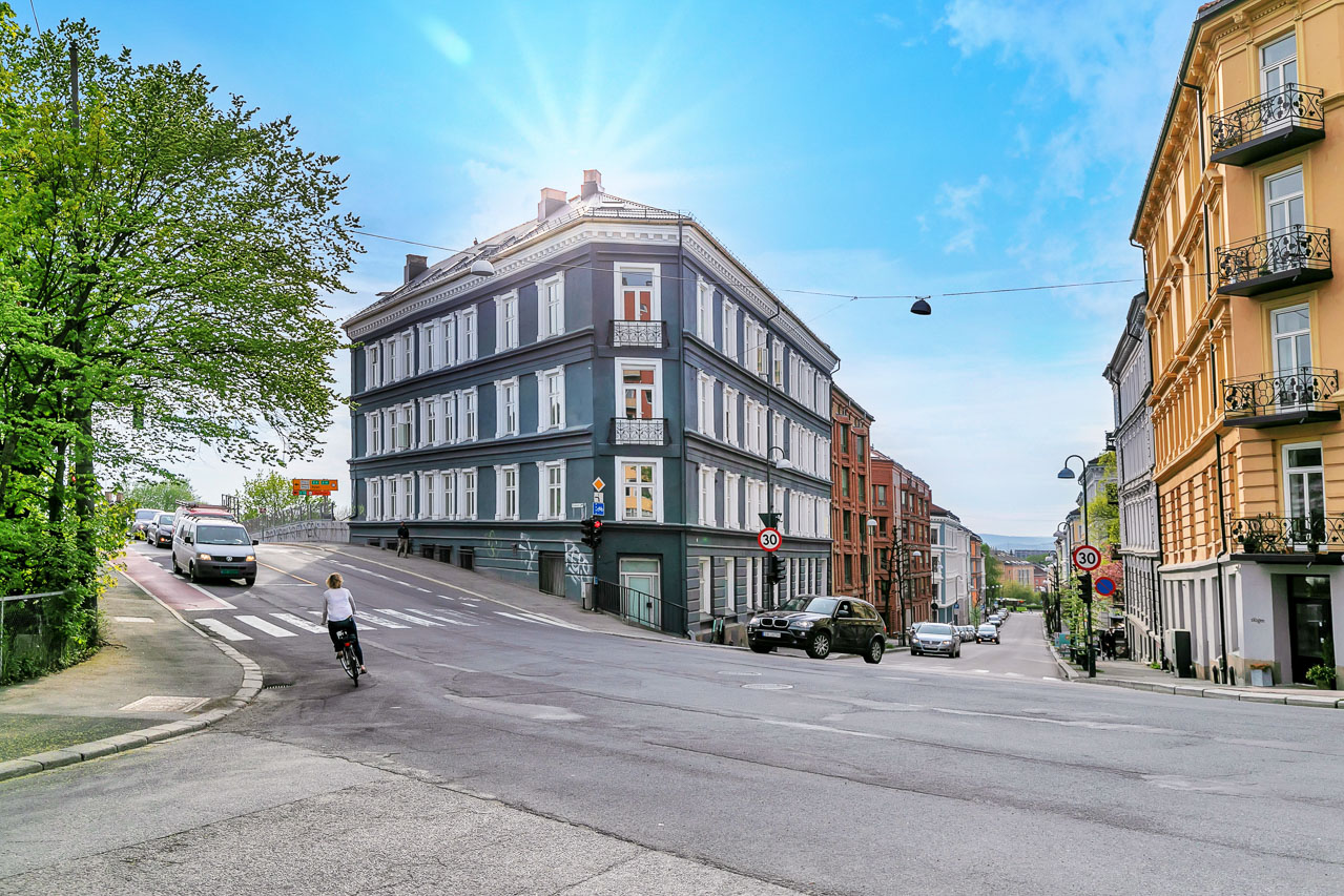 Klassisk bygård på hjørnet i Oslo med trikkeskinner og blå himmel