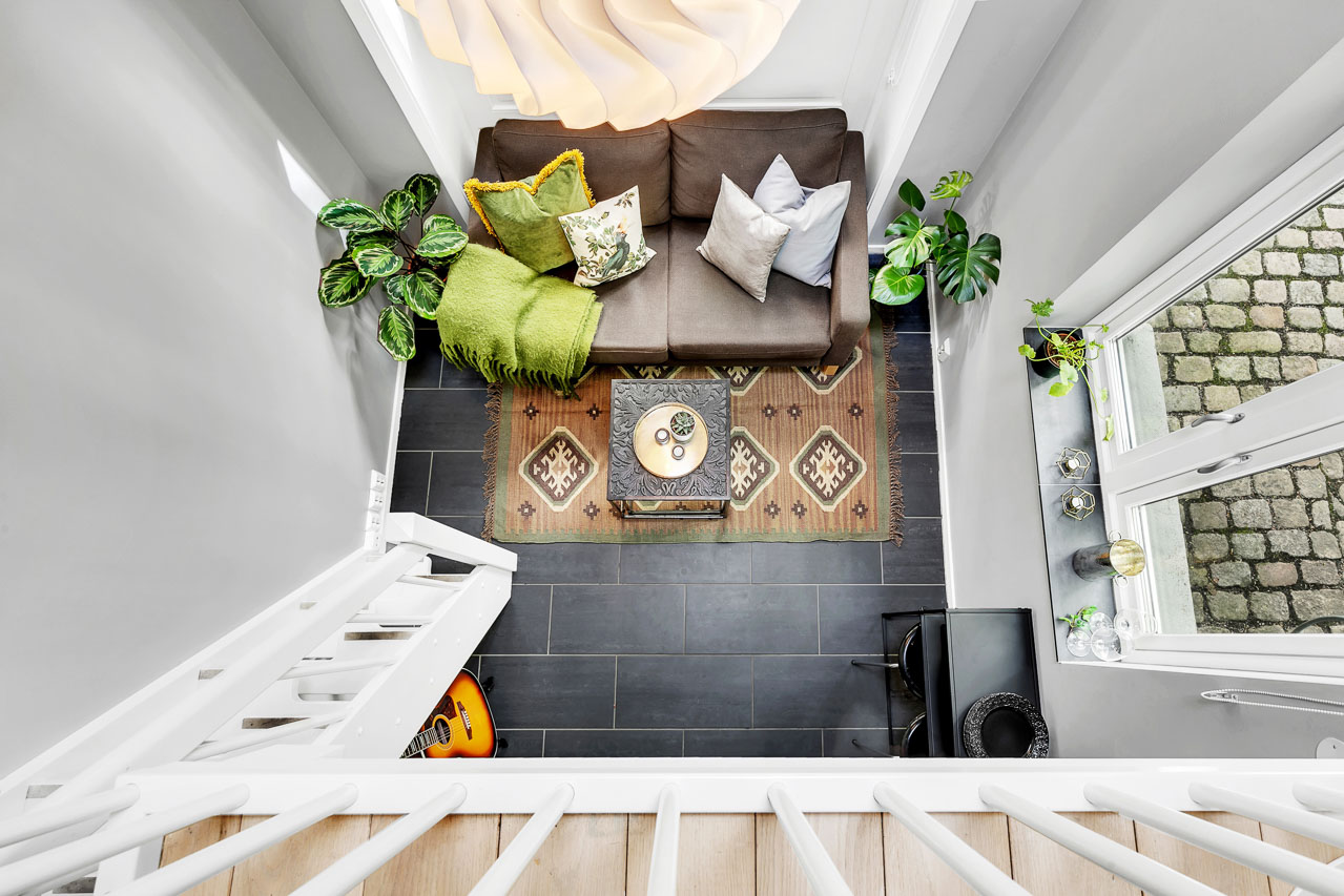 Stue med sofa, teppe og planter fotografert ovenfra fra mesaninen