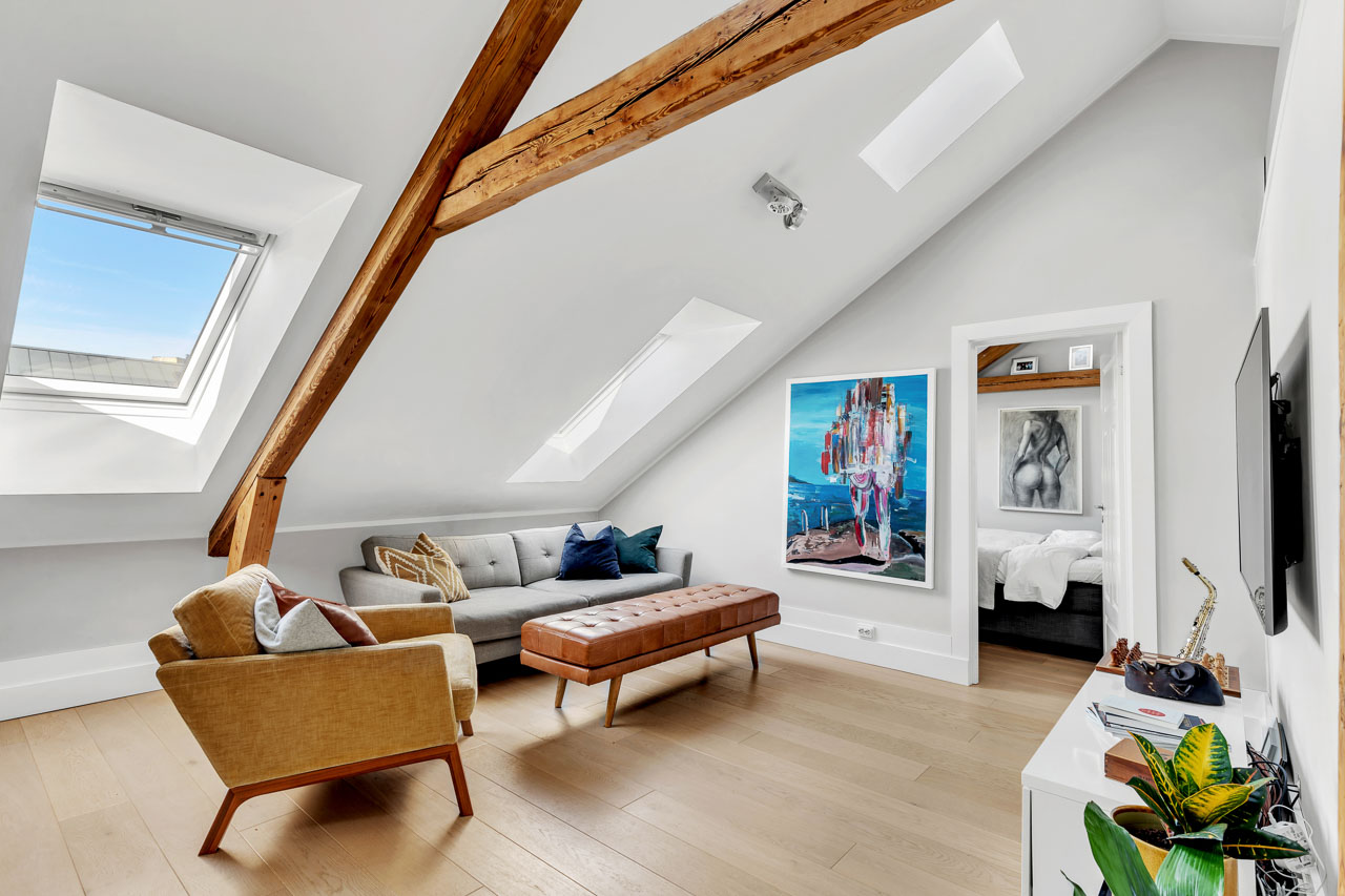 Loftstue med sofa, takvindu og kunst på veggen i mykt dagslys