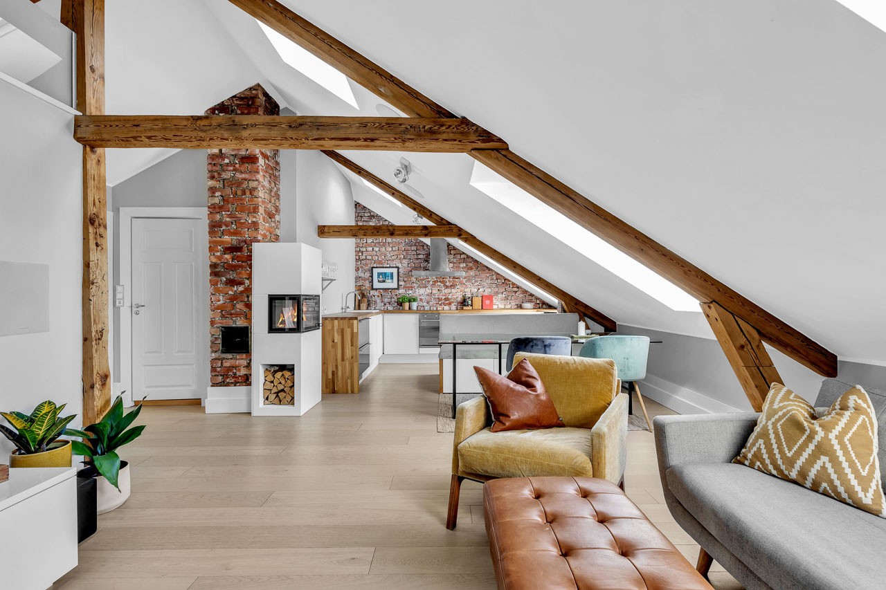 Loftsleilighet med teglvegg, synlige bjelker og skinnsofa i stua